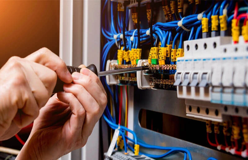 Electrician's hands working on an electrical panel with screwdriver, connecting wires to terminals