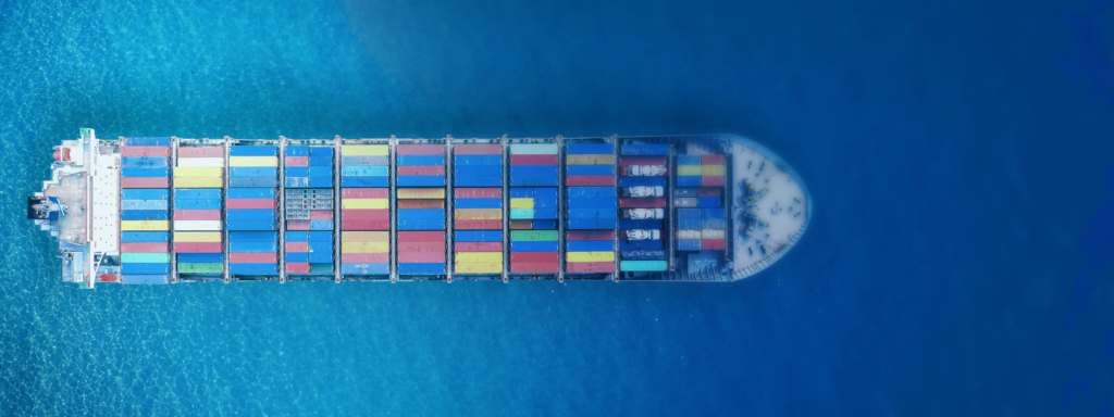 Aerial view of a fully-loaded container ship navigating through blue waters, highlighting the vibrant array of shipping containers on deck, illustrating the vast scope of global trade and maritime logistics.